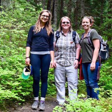 Kat, Catherine and Hannah stand on the Winner Creek Trail in Girdwood with lots of green leaves