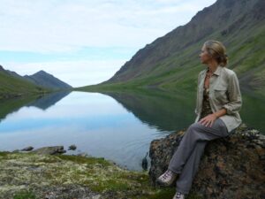 Marybeth sitting in front of a long lake with reflection of mountains.