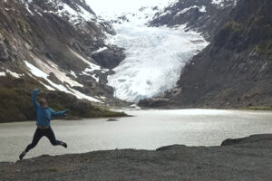 Michelle's jumping in front of a lake with a glacier in the background.