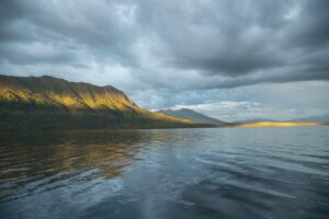 Sunshine on a ridge across the river water with cloudy skies.