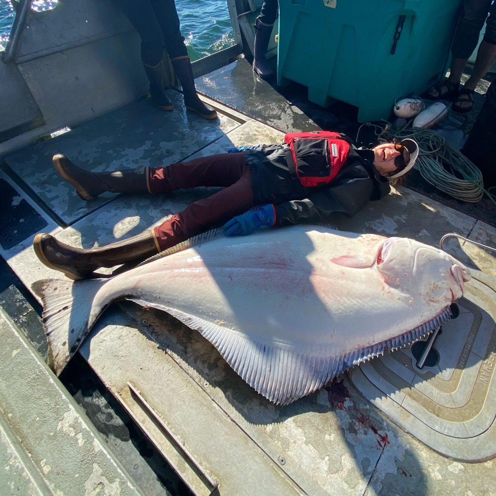 Suzanne gets outside into tidepools to tussocks, and here lays next to a 166-lb halibut she caught in 2022. 